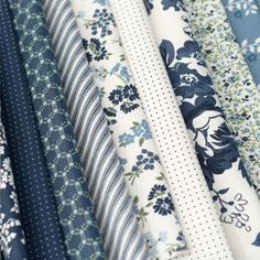 many different types of fabrics are stacked together in this close up photo, with one blue and white flowered design on the fabric