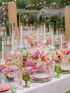 the table is set with pink and white flowers, candles, plates and napkins