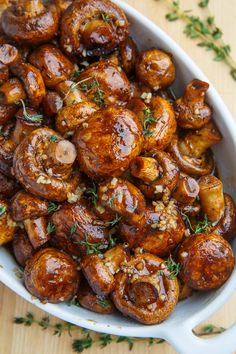 a white bowl filled with cooked mushrooms and garnished with herbs