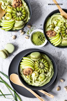 two bowls filled with green smoothie topped with kiwi and nuts next to spoons