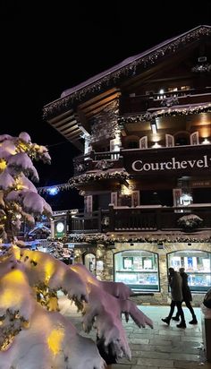 people are walking on the sidewalk in front of a building covered with snow at night