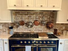 a kitchen with an oven, stove and pots hanging on the brick wall above it