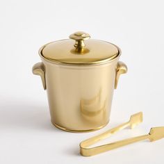 a gold pot and tongs on a white surface