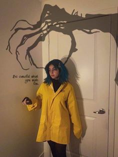 a woman with blue hair standing in front of a door wearing a yellow raincoat