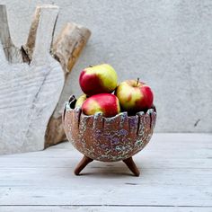 a bowl filled with apples sitting on top of a wooden table