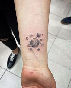 a small tattoo on the wrist of a woman's arm with planets and stars