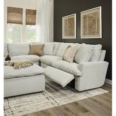 a large white sectional couch in a living room with pillows on the back and footstools