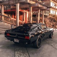 a black muscle car parked in front of a large wooden building with steps leading up to it