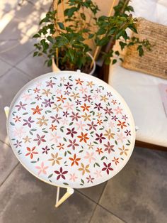 a white table with flowers painted on it and a potted plant in the background