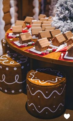 gingerbread houses are sitting on top of small stools in front of a christmas tree