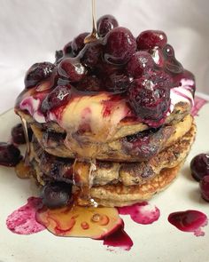 a stack of pancakes with blueberries and syrup drizzled over them on a white plate