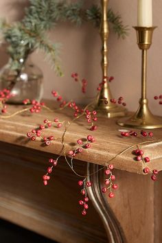 a mantle with candles and red berries on it, next to a candle holder filled with greenery