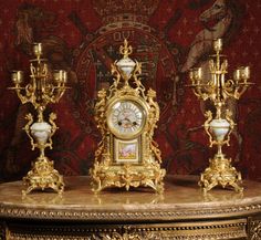 an ornate gold clock and candelabra set in front of a red wall