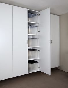 an empty room with white cupboards and plastic bins in the middle, on top of carpeted flooring