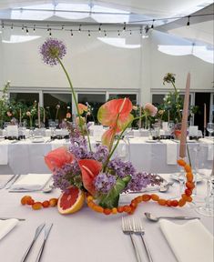 an arrangement of flowers and fruit on a table in a banquet hall with white linens