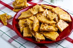 a red plate topped with pieces of tofu next to pine cones on a checkered table cloth