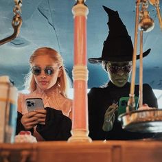 two people dressed as witches are looking at their cell phones in front of a mirror