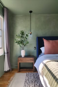 a bed sitting next to a window with a plant on it's side table