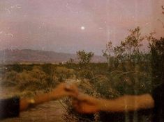 two hands reaching out towards each other in front of a desert landscape with hills and trees