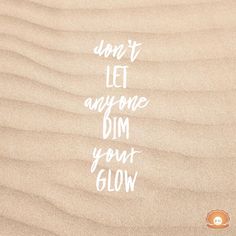 the words don't let anyone dim your glow are written in white on sand