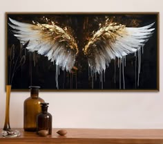 a painting with white and gold wings hanging on a wall above a table next to bottles