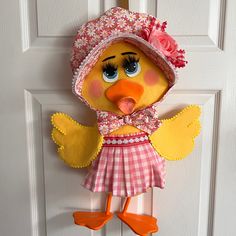 a stuffed bird wearing a pink dress and hat hanging on a door handle with orange rubber shoes