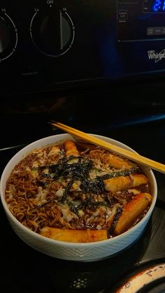 a bowl of noodles with chopsticks sitting on top of an oven burner