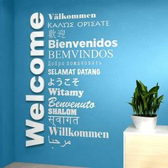 a blue wall with the word welcome written in different languages on it and a potted plant next to it