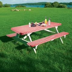 a picnic table in the middle of a grassy field with bottles and food on it