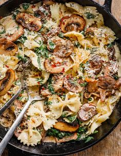 a skillet filled with pasta, mushrooms and spinach on top of a wooden table