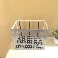 a metal basket sitting on top of a white table next to a potted plant