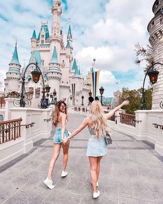 two young women are walking in front of a castle with their arms out to each other