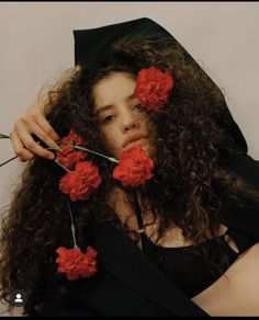 a woman with long curly hair wearing a black graduation cap and holding red flowers in her hair