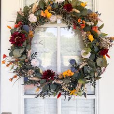 a wreath hanging on the front door of a house with flowers and leaves around it