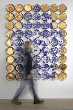 a woman walking past a large blue and white wall sculpture with gold plates on it