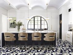 a kitchen with black and white tile flooring next to a counter top island topped with four beige bar stools