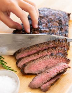 a person cutting up some meat on a wooden cutting board with a knife and seasoning