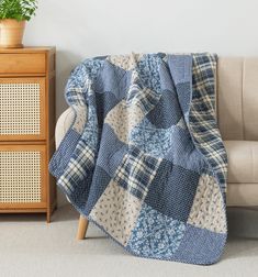 a couch with a blue and white quilt on it next to a potted plant