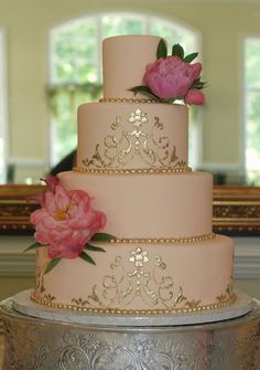 a three tiered cake with pink flowers on the top and silver icing, sitting on a table