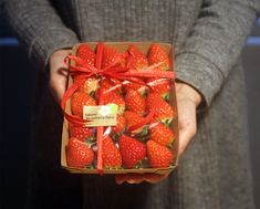 a person holding a box of strawberries with a red ribbon around the bow on it