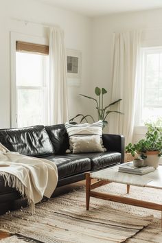 a living room with black leather couches and white curtains