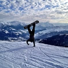 a man doing a handstand on top of a snow covered slope with his snowboard