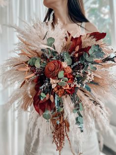 a woman holding a bouquet with feathers and flowers