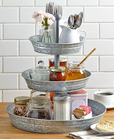 three tiered tray with jars and utensils in them on top of a wooden table