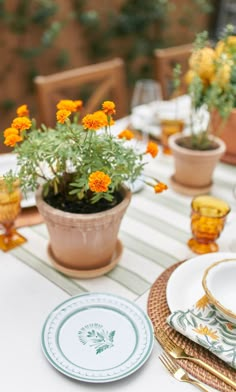 the table is set with plates and flowers in pots on it, along with other place settings