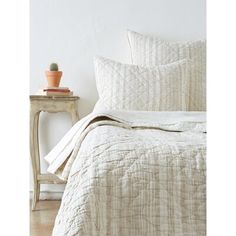 a white bed with two pillows and a small potted plant on the end table