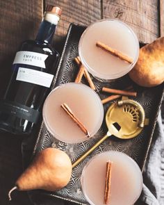 two glasses filled with drinks and cinnamon sticks on a tray next to a bottle of wine