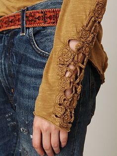 a person wearing jeans and a brown shirt with an intricate lace design on the sleeves