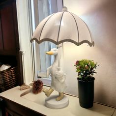 a white duck lamp sitting on top of a table next to a potted plant