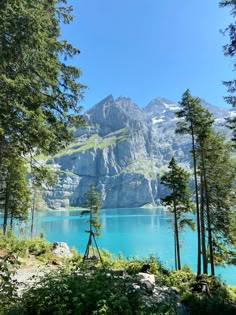 a lake surrounded by trees and mountains with blue water in the foreground on a sunny day